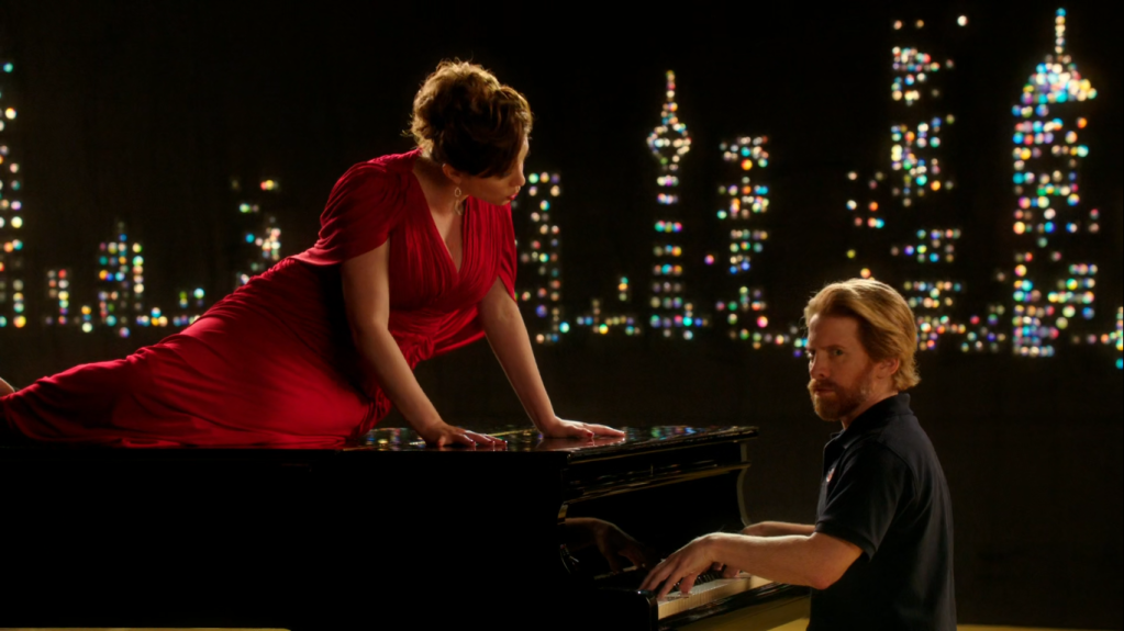 crazy ex-girlfriend rebecca wears a red dress and sings atop a piano as patrick the delivery man plays the piano